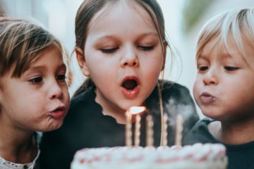 Kinder beim Auspusten von Kerzen auf einem Geburtstagskuchen